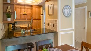 A kitchen with wooden cabinets, a built-in island, pendant lights, and a clock on the wall. - Gorgeous Ground Floor Condo in World Class Resort, Pool, Spa, Amenities Galore! (Naples)