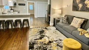 A modern living room with a gray sofa, a yellow ottoman, and a patterned rug. - Greer Twin Cottage A - Walk to City Park and Downtown Greer (Greer)