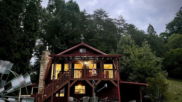 A two-story log cabin with a balcony, surrounded by trees. - Rock Right Inn* Cozy /Mtn Views*Creek*Firepit*Hot tub*1.5 acres* 4bed/2 bed*8-10 (Cosby)