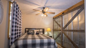 A bedroom with a checkered bedspread, a ceiling fan, a wooden-framed window, and a nightstand with a lamp. - Rock Right Inn* Cozy /Mtn Views*Creek*Firepit*Hot tub*1.5 acres* 4bed/2 bed*8-10 (Cosby)