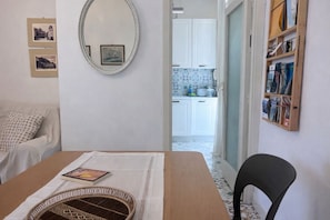 A room with a dining table, a chair, a mirror, and a bookshelf.