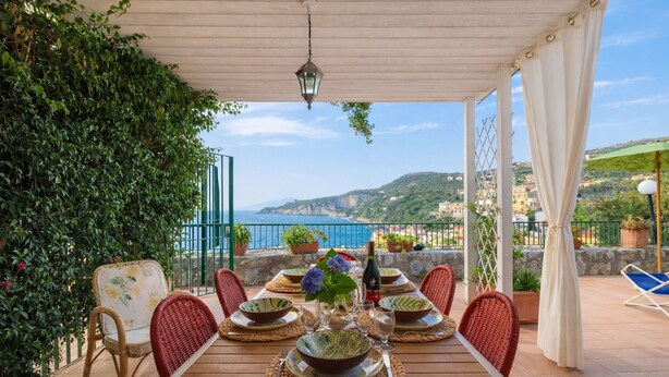 Un espace de restauration en plein air avec vue sur la mer, des chaises en osier et une table dressée pour deux personnes.