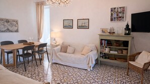 Un salon comprenant une table à manger, des chaises, un canapé, une bibliothèque et un lustre.