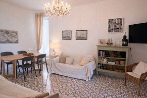 A living room with a dining table, chairs, a sofa, a bookshelf, and a chandelier.