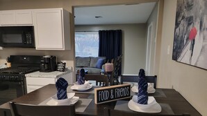 Un comedor con un letrero que dice "FOOD & FRIENDS", una cocina con cafetera y una sala de estar con sofá y ventana con persianas.
