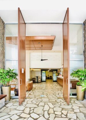 Un hall d’entrée avec un sol carrelé en pierre, des portes en bois et des plantes en pot.