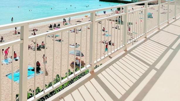 Vue sur la plage depuis un balcon doté d’une balustrade, avec un ciel dégagé et le profil de la ville en arrière-plan.