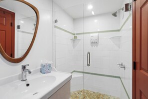 Ein Badezimmer mit Waschbecken, Spiegel, Duschabtrennung aus Glas und Tür.