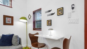 Ett kompakt vardagsrum med en soffa, två fåtöljer, ett litet bord, en golvlampa, ett fönster med persienner och väggmonterade eluttag.