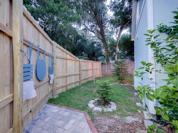 A backyard with a wooden fence, a small tree, and a brick pathway.