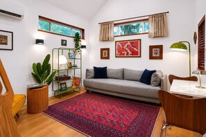 Ein Wohnzimmer mit grauem Sofa, einem roten Teppich mit Muster, Holzmöbeln und Bildern an den Wänden.
