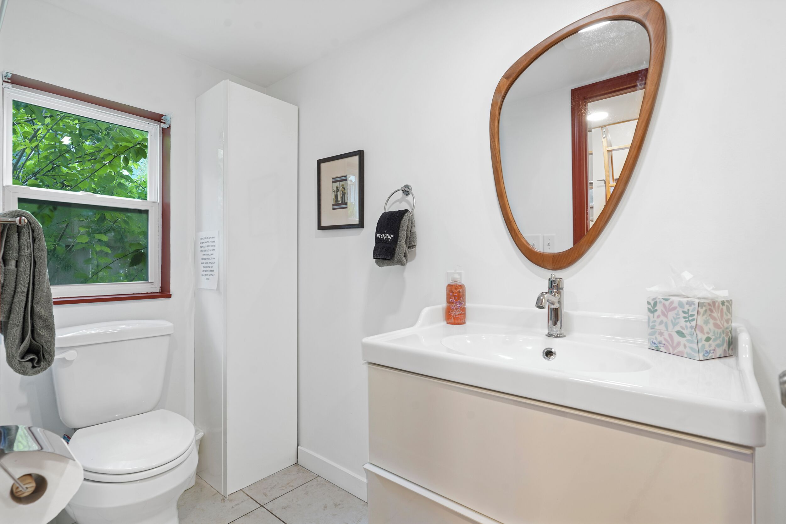 A bathroom with a toilet, sink, mirror, window, and towel rack.