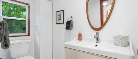 A bathroom with a toilet, sink, mirror, window, and towel rack.