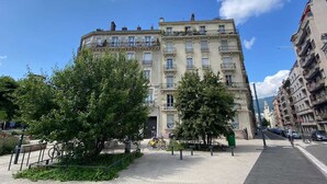 Un immeuble à plusieurs étages doté de balcons, d’une promenade piétonne et d’arbres.