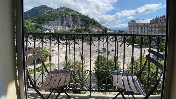 Un balcon doté de balustrades en fer forgé et de deux chaises en bois.