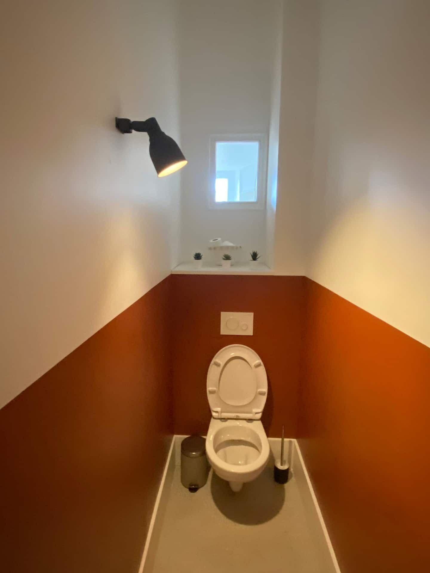 A small bathroom with a toilet, a hand dryer, and a window.