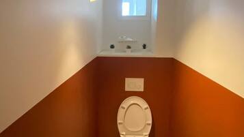 A small bathroom with a toilet, a hand dryer, and a window.