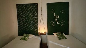 Une pièce avec deux lits, chacun recouvert d’une couverture verte et agrémenté d’un oreiller. Deux tableaux noirs sont accrochés aux murs, et une lampe est suspendue au plafond.