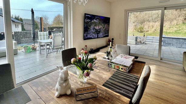 A modern living room with a large TV, a wooden coffee table, and a glass door leading to a patio.