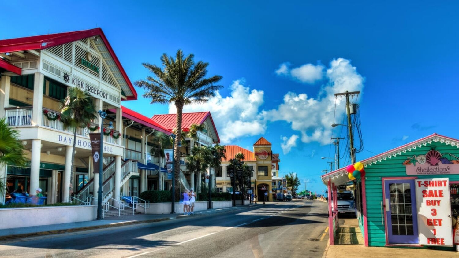 Vista de la calle con un hotel llamado 'Kirk Freeport' y una tienda con un cartel de venta de camisetas.
