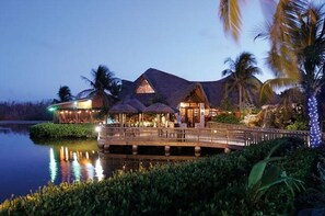 A resort with a thatched-roof building, a wooden deck, and a body of water. - Ocean Front Divers Haven - World Class Diving & Snorkeling One Giant Stride Away (West Bay)