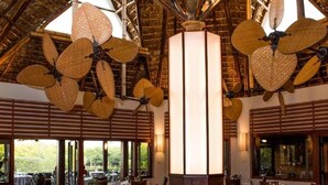 Un restaurant avec de hauts plafonds, de grands ventilateurs en osier et des tables dressées pour le dîner.