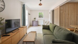 A modern living room with a flat-screen TV, wooden cabinet, green sofa, and a small table. - Large apartment with terrace and pool view (La Bouilladisse)