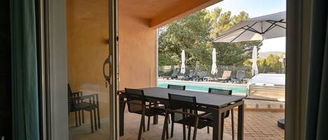 A patio with a table and chairs, a pool, and umbrellas in the background.