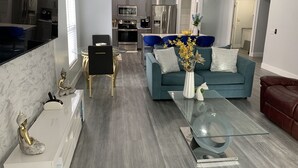 Una sala de estar moderna con una mesa de centro de vidrio, un sofá azul y un comedor con una mesa y sillas de vidrio.