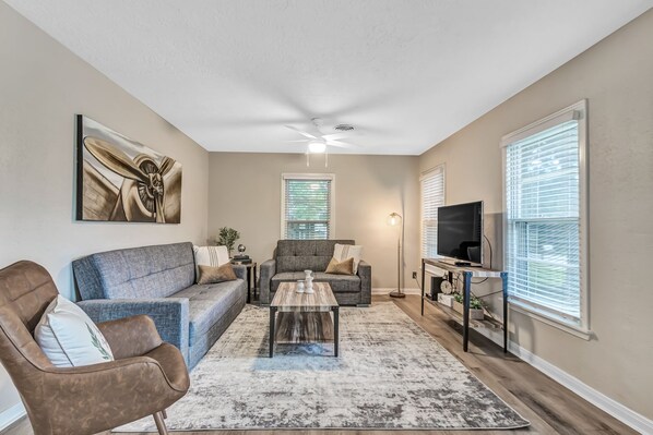 A living room with a sofa, armchair, coffee table, TV, and artwork.