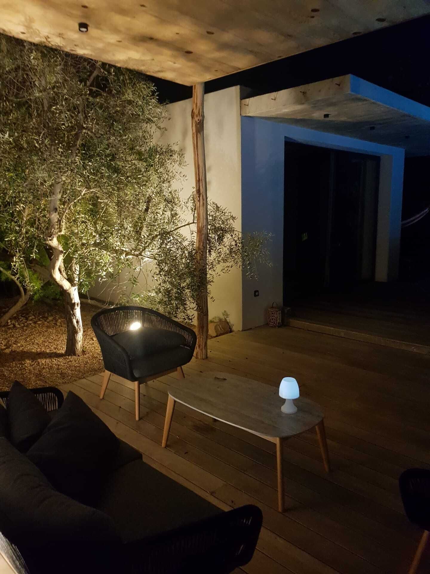 Un espacio exterior con asientos, un sofá y una mesa, rodeado de árboles y una estructura de edificio moderna.