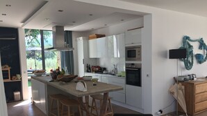 Een moderne keuken met een centraal eiland, houten krukken en uitzicht op de omgeving.