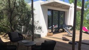 Een houten terras met buitenmeubilair, een overdekt gedeelte met een glazen deur en uitzicht op een zwembad.