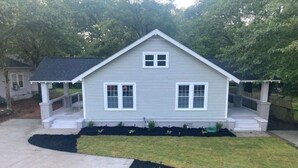 Une maison de plain-pied avec un toit à pignon, une véranda et un jardin aménagé devant la maison, ainsi qu’une allée en béton.
