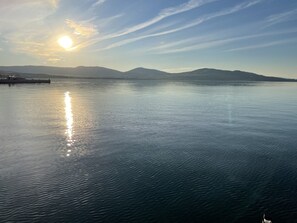 Une étendue d’eau calme où se reflète le soleil, avec des montagnes lointaines et une jetée sur la gauche.