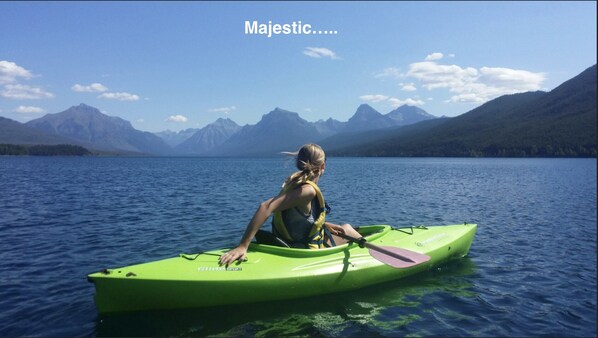 Une personne pratiquant le kayak sur un lac paisible, avec des montagnes en arrière-plan.