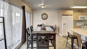 A dining area with a table, chairs, a clock, and a kitchen with appliances.
