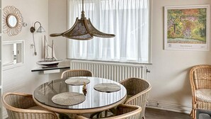 A dining area with wicker chairs, a glass table, and a ship model on a shelf.
