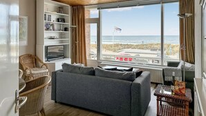 A living room with a large window, a bookshelf, a grey sofa, and a wicker chair.