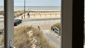 A beach view from inside a building, with a parking area and a pedestrian path leading to the beach.
