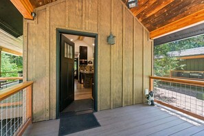 Fachada de madera con una puerta que da a un espacio interior, un balcón con barandilla y vistas al verdor.