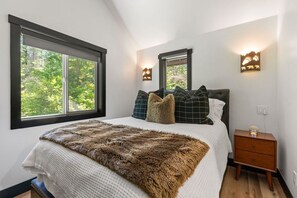 Un dormitorio con una cama grande, dos mesitas de noche y una ventana con vistas a árboles.