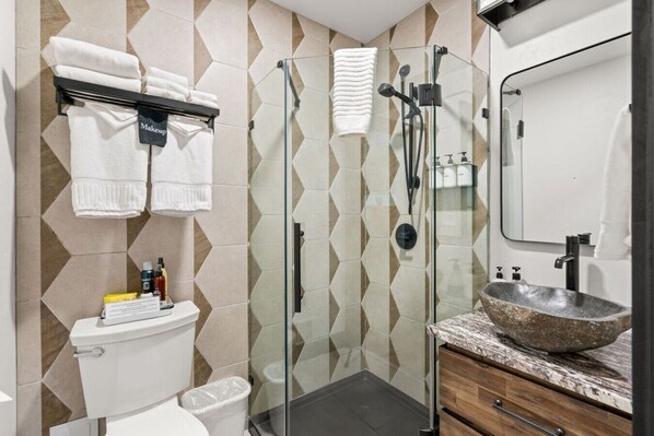 A modern bathroom with a glass shower enclosure, a white toilet, a vanity with a stone basin sink, and a towel rack with neatly folded towels.