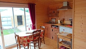 A wooden cabin with a dining area, kitchen, and sliding glass doors to a backyard. - Studio in a chalet (Bourlon)
