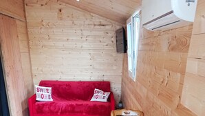 A wooden interior with a red sofa, a wooden table with a remote, and a small potted plant. - Studio in a chalet (Bourlon)