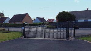 A gated driveway leading to a residential area with houses and a stop sign. - Studio in a chalet (Bourlon)