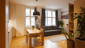 Ein modernes Wohnzimmer mit einer Couch, einem Esstisch und Stühlen. Ein großes Fenster mit Vorhängen, eine Stehlampe und ein Blumentopf sind ebenfalls vorhanden.
