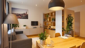 Ein modernes Wohnzimmer mit einer Couch, einem Esstisch und einem Fernseher. Pflanzen und eine Lampe sind ebenfalls vorhanden.