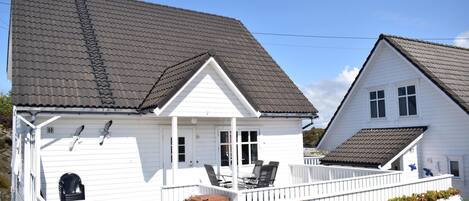 Two white houses with grey tiled roofs, a porch with chairs, and a small garden area.