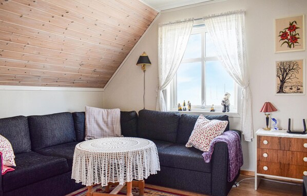A cozy living room with a dark grey sofa, a round white crochet table, and a wooden ceiling.
